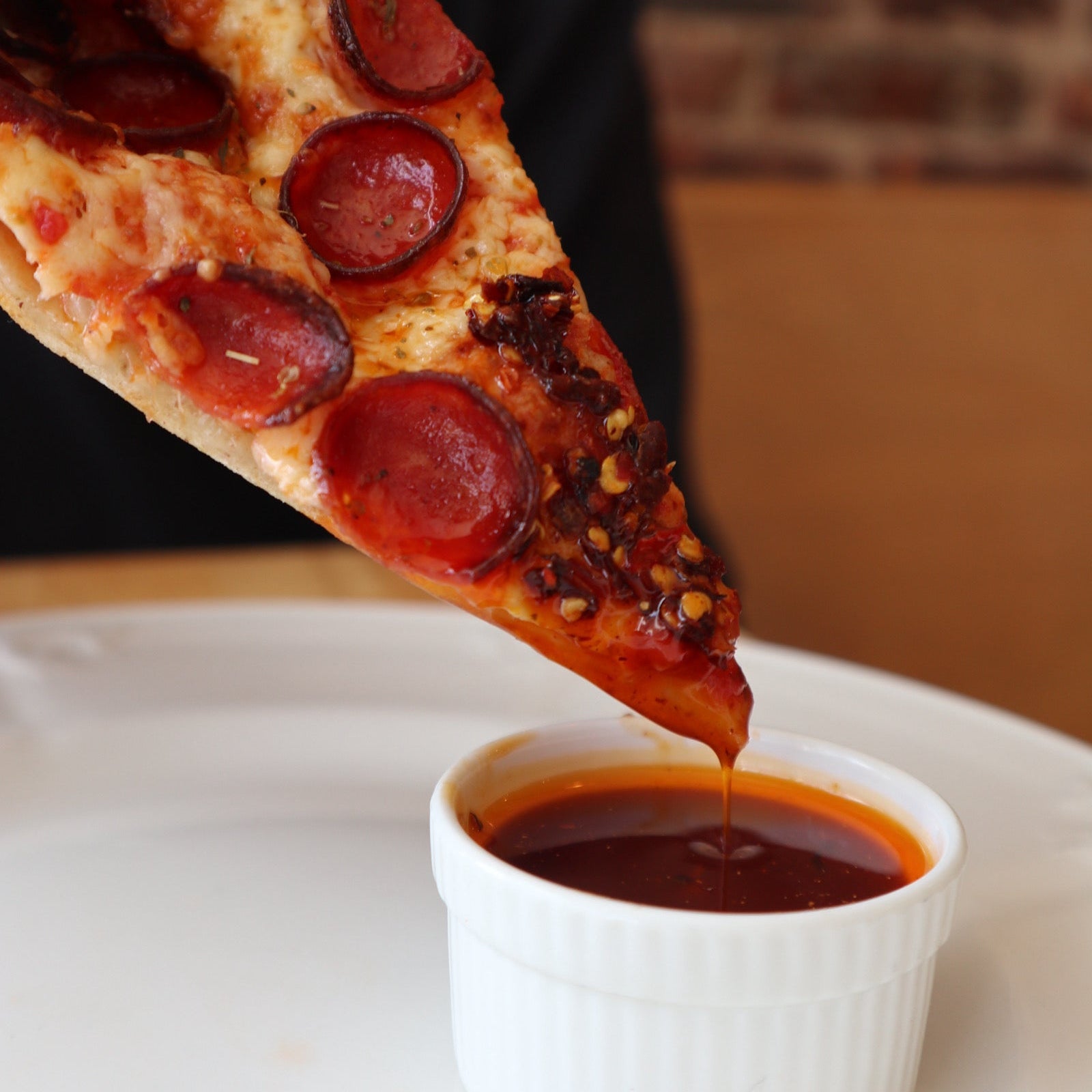 Pizza slice with pepperoni being drizzled with Chili Crisp from a white container.